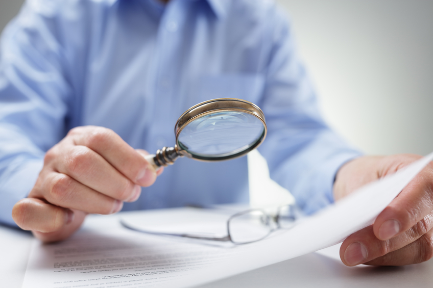 Image of a man with a magnifying glass. Learn about how a professional employer organization helps businesses.