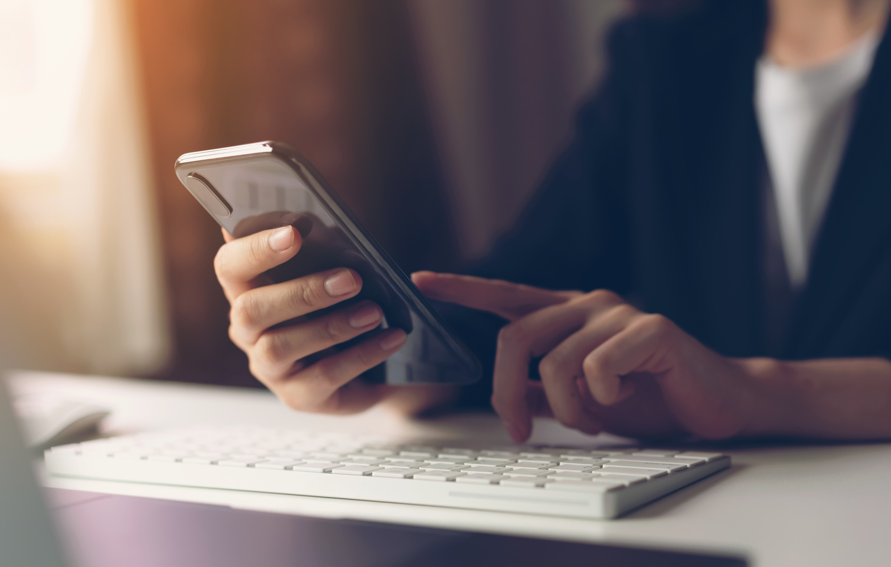 A small business owner in Georgia using a smart phone and computer set up with proper cybersecurity practices.