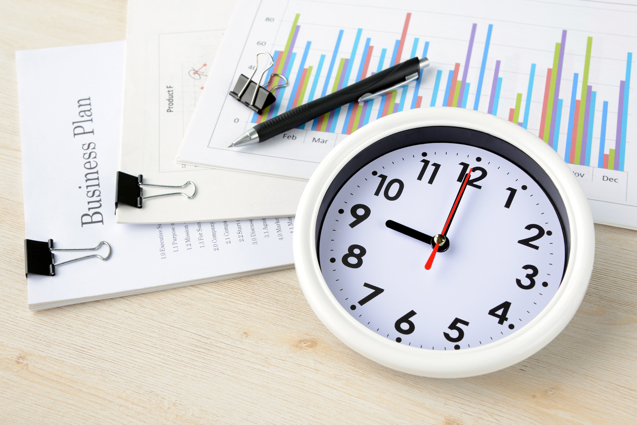A clock tracking time for employees now eligible for overtime and papers documenting business numbers like regular rate calculations.