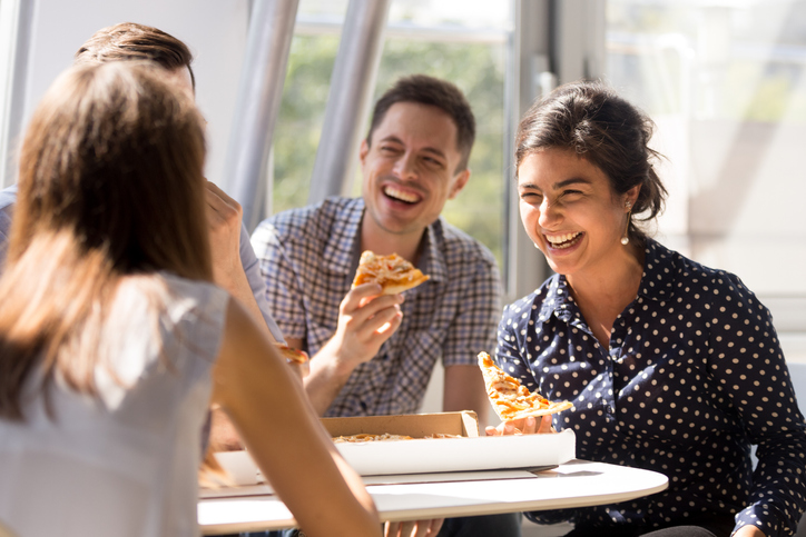 A group of coworkers are enjoying a pizza together at the office during lunch.